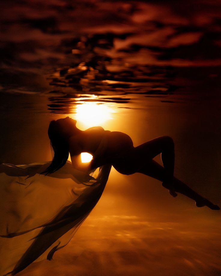 a woman is floating in the water at sunset