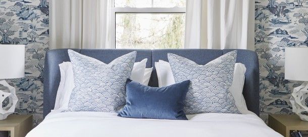 a bedroom with blue and white wallpaper and pillows on the bed, along with two lamps