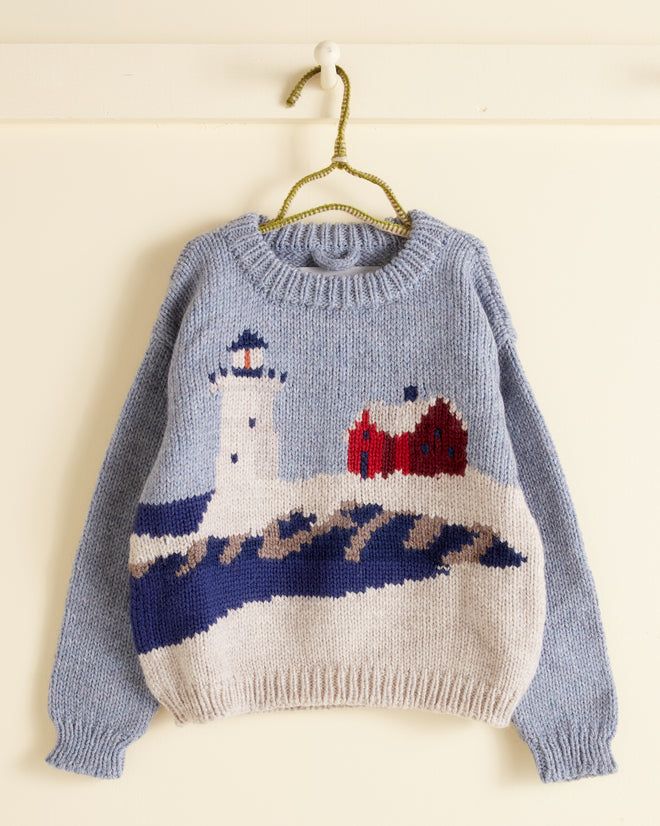 a sweater hanging on a clothes hanger with a house and lighthouse in the background