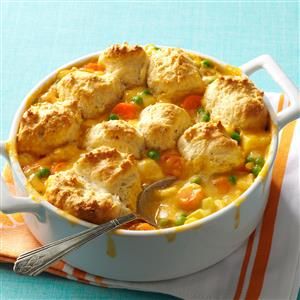 chicken pot pie with biscuits and carrots in a white casserole dish on a blue tablecloth