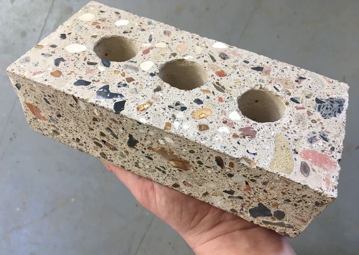 a hand holding up a small brick with two holes in it's center and several different colored rocks on the outside