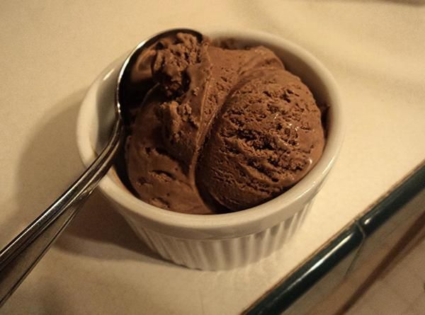 two scoops of chocolate ice cream in a bowl with a spoon next to it