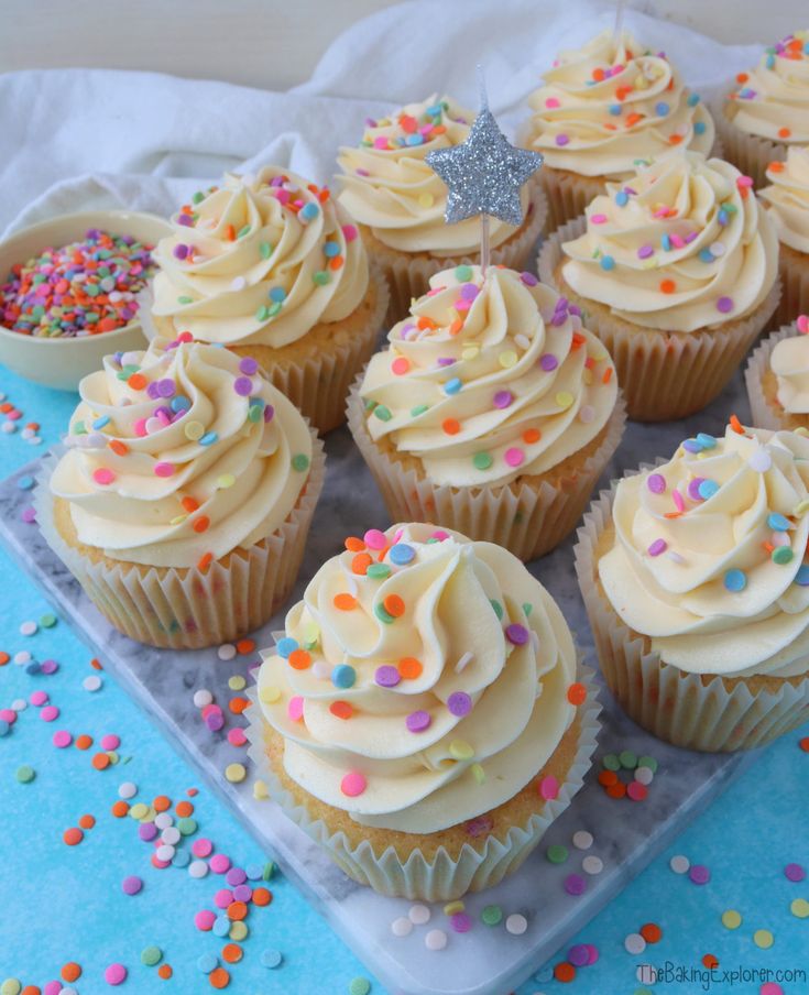 cupcakes with white frosting and sprinkles on a tray