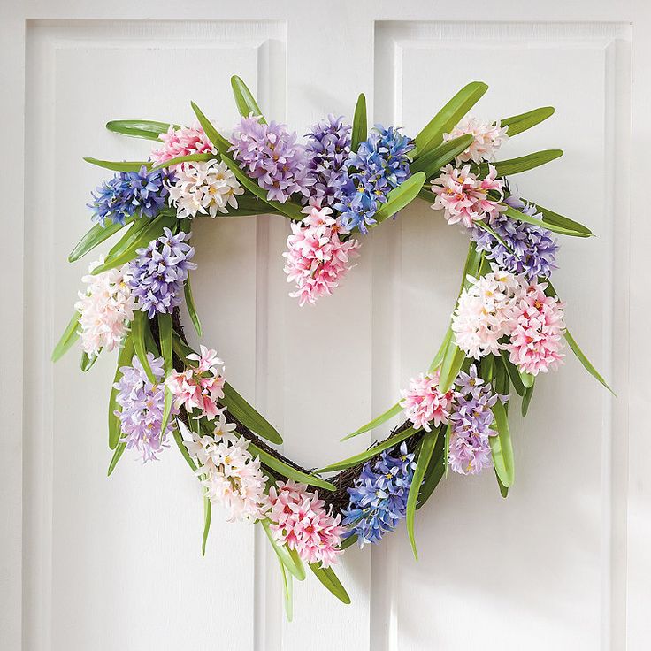 a heart shaped wreath with purple and pink flowers on it hanging from a white door