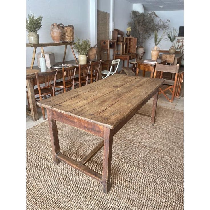 a wooden table sitting on top of a rug next to chairs and potted plants