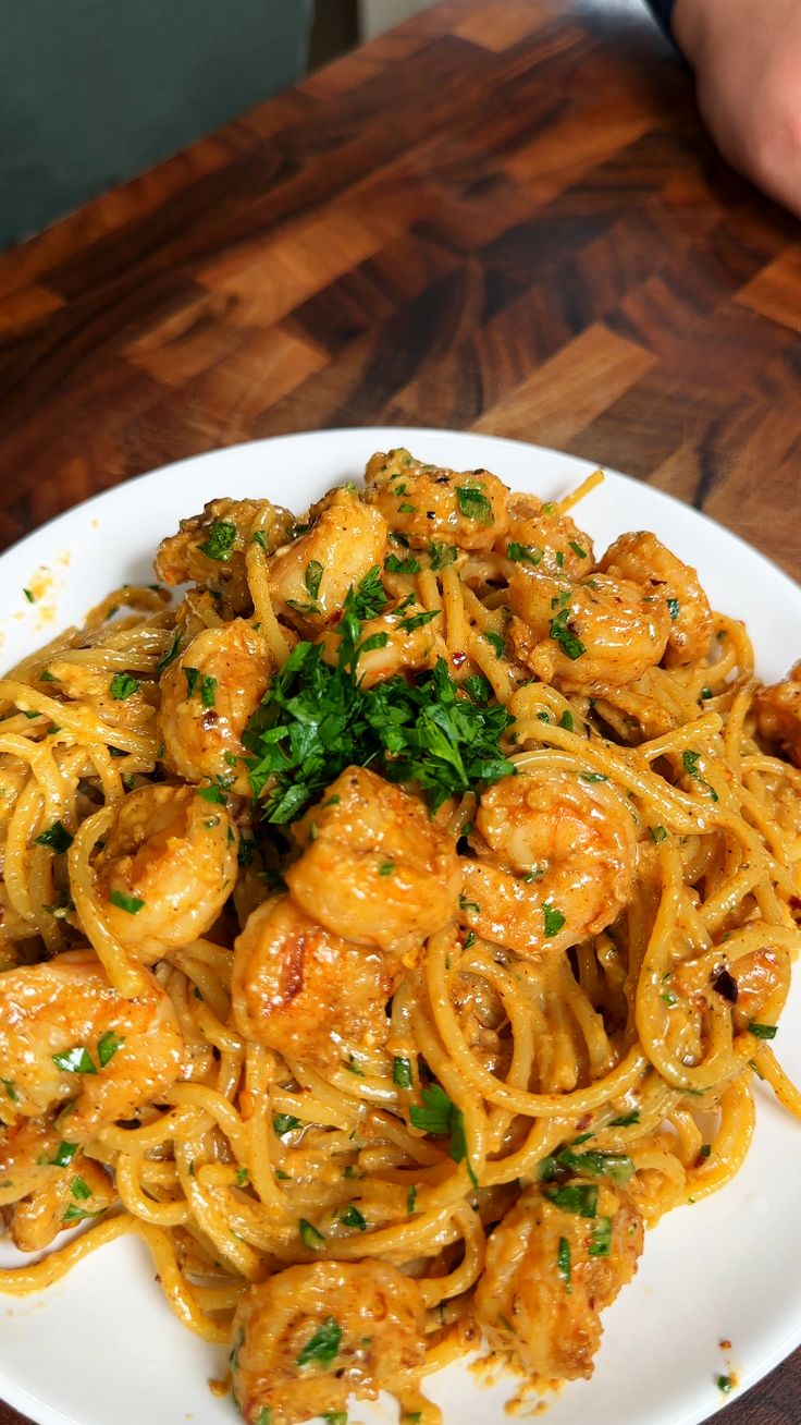 a white plate topped with pasta covered in shrimp and garnished with parsley