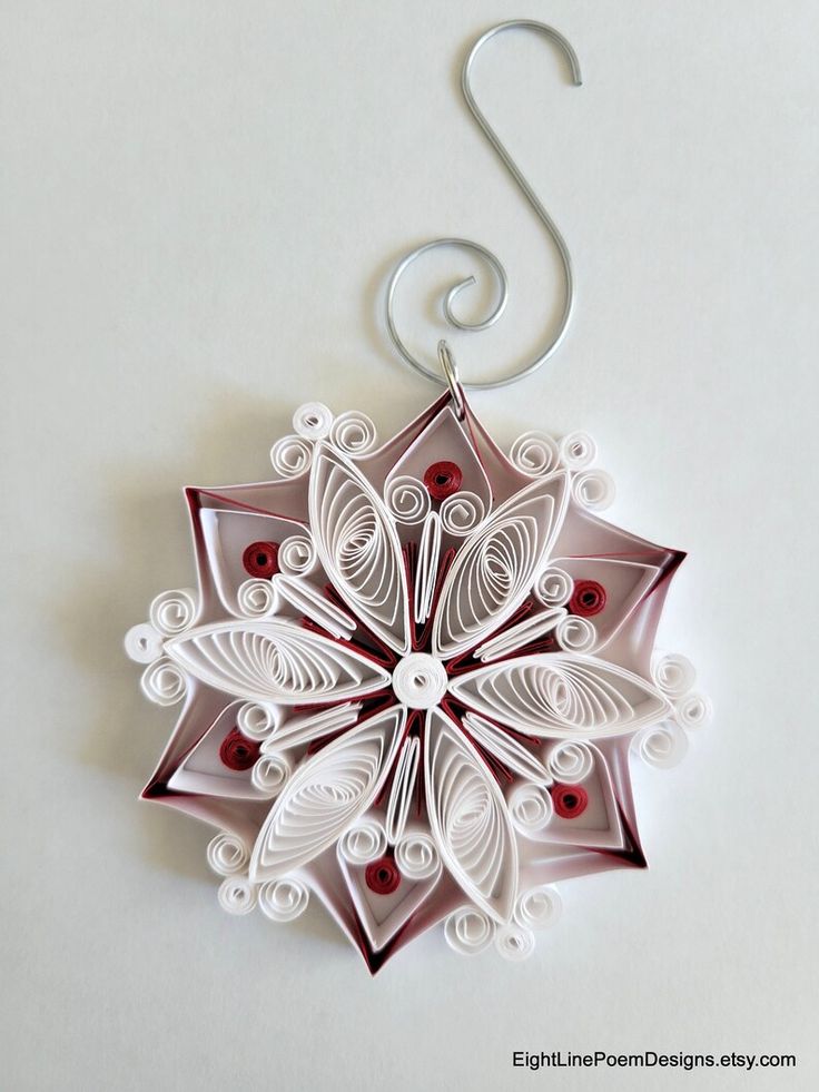 an ornament made out of white paper with red beads and a metal hook