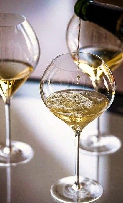 three wine glasses filled with white wine being poured