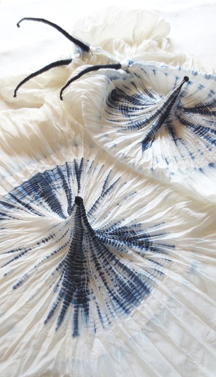 two blue and white fan shaped objects laying on top of a bed covered in sheets