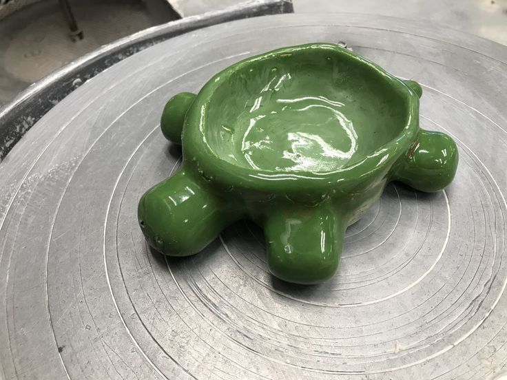 a green ceramic turtle shaped bowl sitting on top of a metal tray in the shape of a turtle