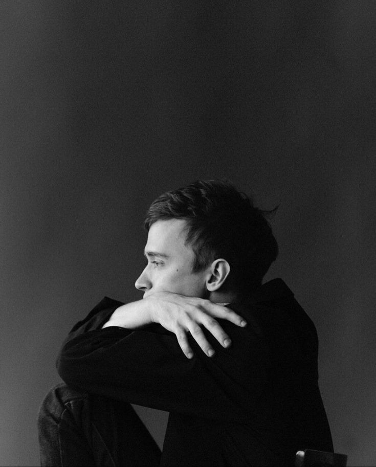 a black and white photo of a man with his hands on his face sitting down