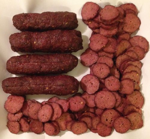 several sausages and potatoes are on a white plate, ready to be cooked in the oven