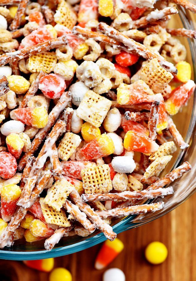 a glass bowl filled with candy corn and cheetos cereal mix on top of a wooden table