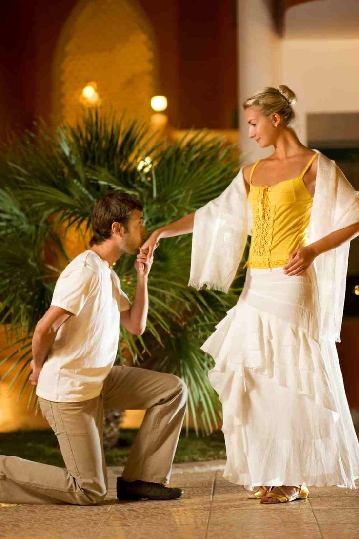 a man kneeling down next to a woman in a white dress and yellow top on the ground