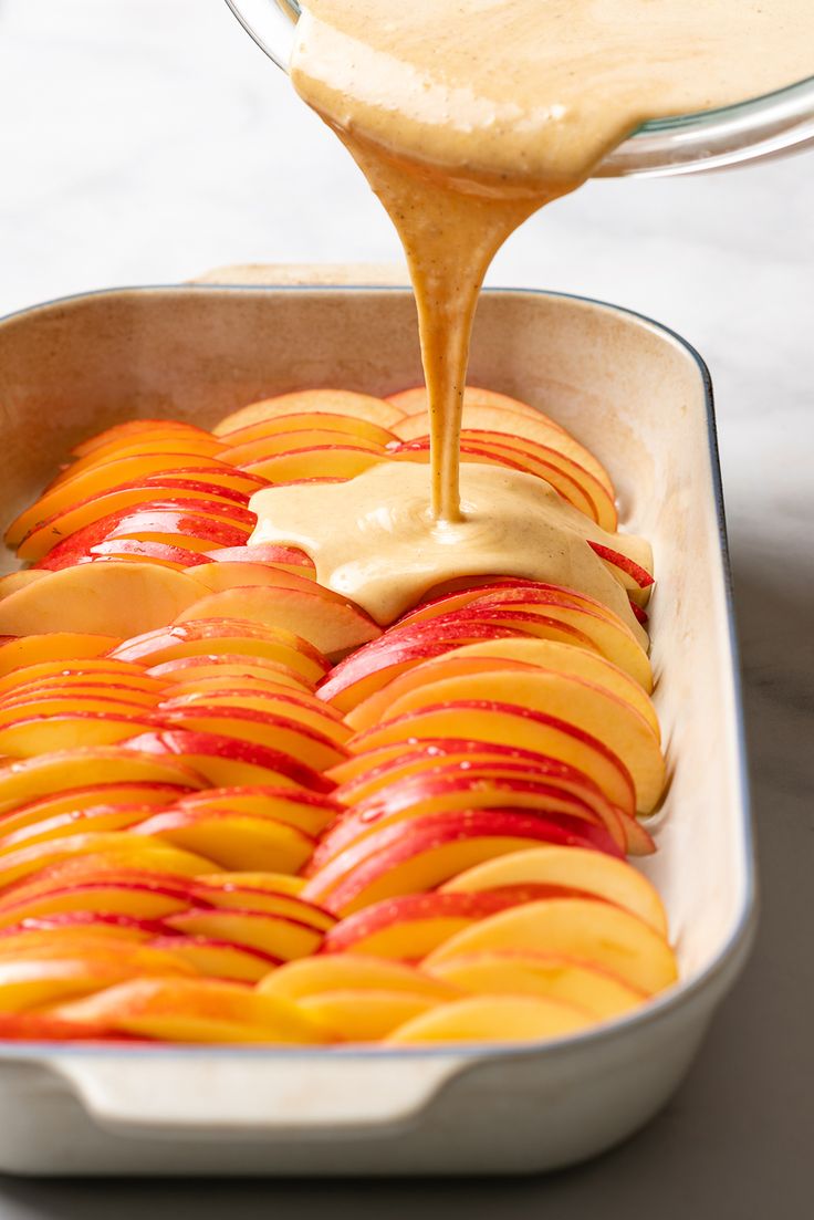 someone pouring caramel sauce on sliced peaches in a baking dish with the rest of the fruit