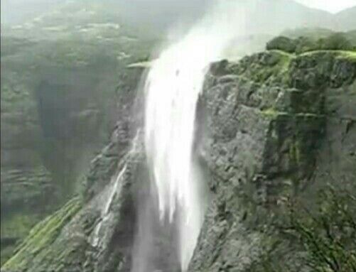 an aerial view of a large waterfall in the middle of a green mountain side area