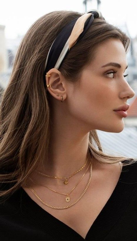 a woman with long hair wearing a black top and gold chain necklace, looking off into the distance