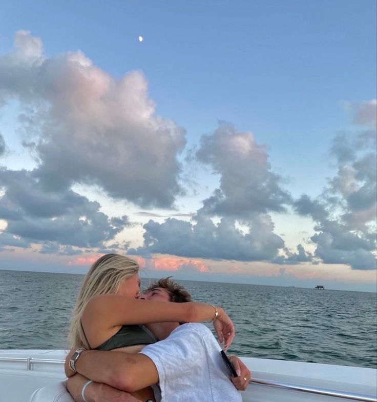 two people embracing each other while on a boat in the ocean at sunset or dawn