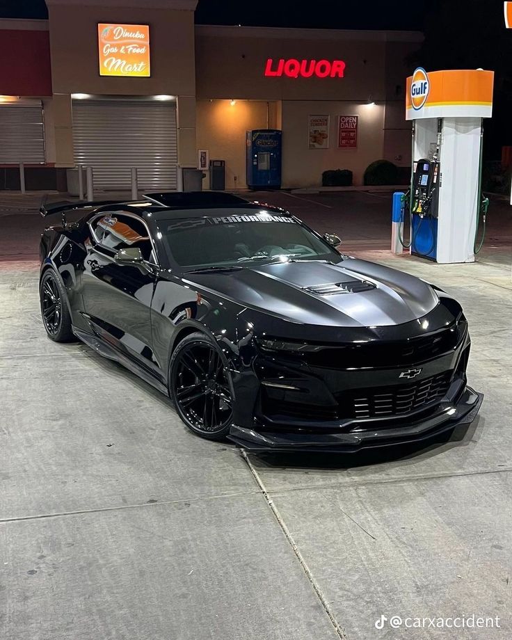 a black chevrolet camaro parked in front of a gas station