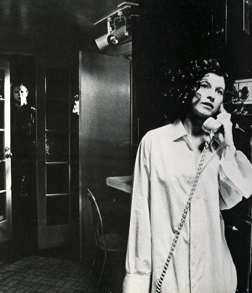 black and white photograph of a woman talking on the phone while standing in a kitchen