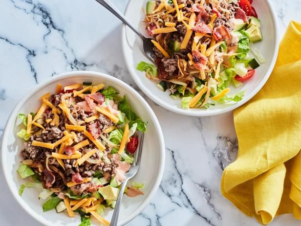 two white bowls filled with salad sitting on top of a marble counter next to yellow napkins