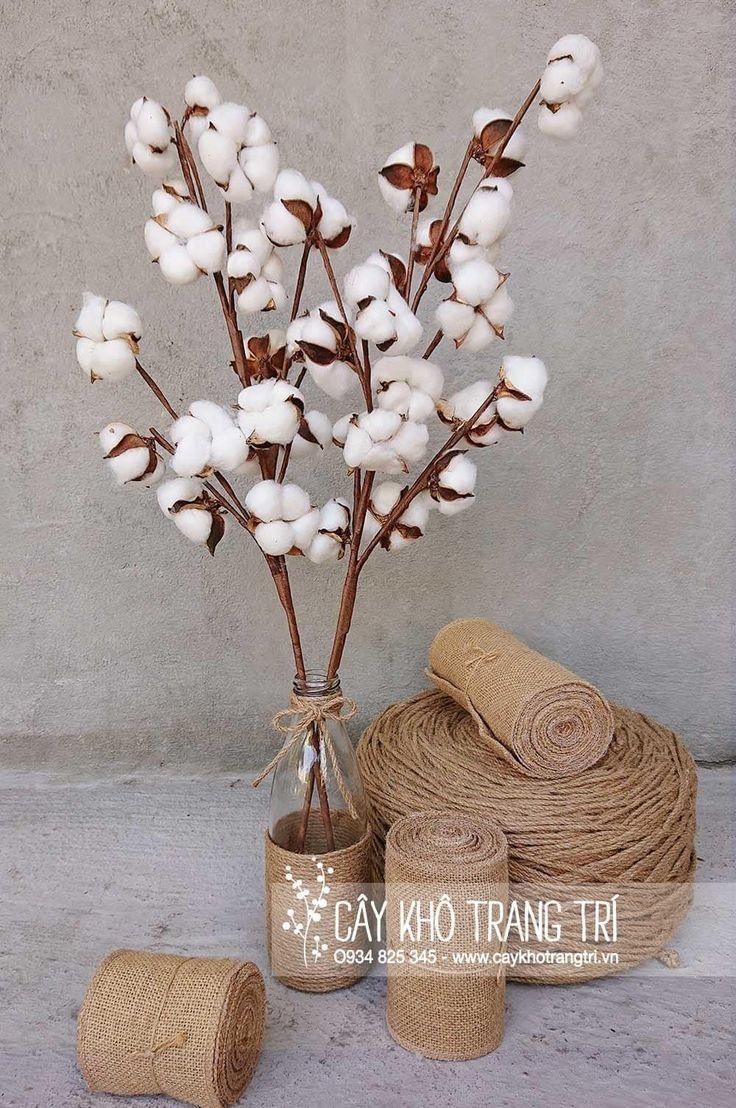 a vase filled with white flowers next to twine and burlocks on the ground