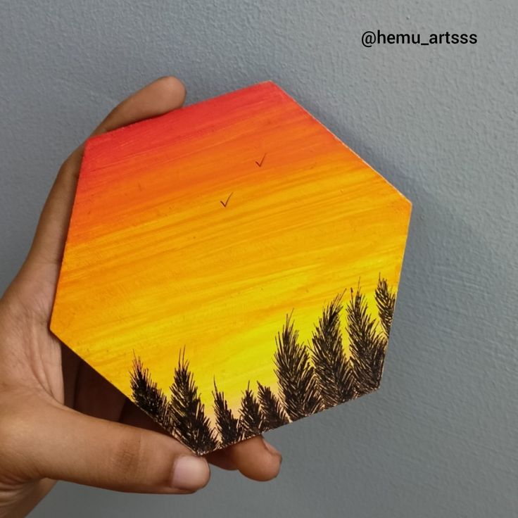 a hand holding up a small wooden box with trees painted on the top and bottom