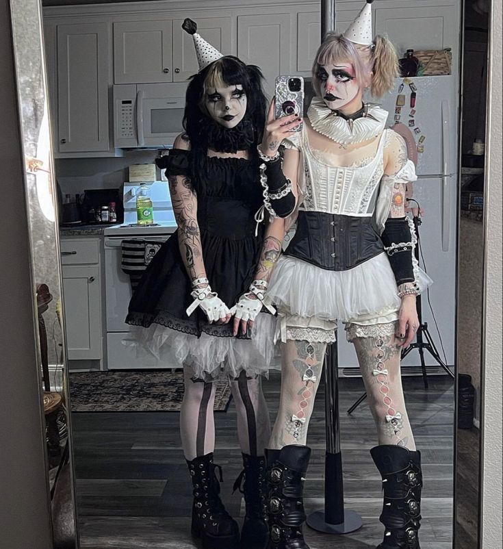 two women dressed up in costumes standing next to each other, one holding a cell phone