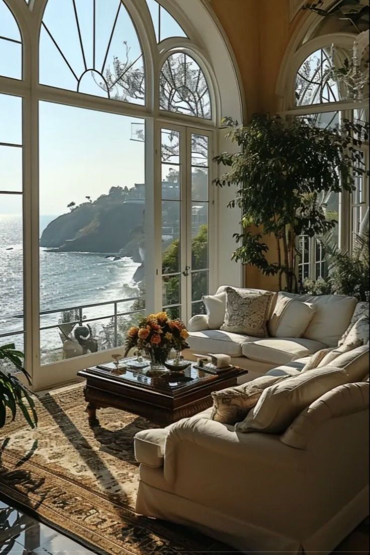 a living room filled with furniture and large windows overlooking the ocean on a sunny day