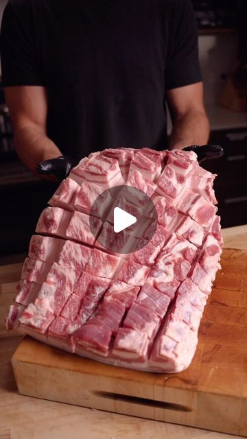 a man standing in front of a wooden cutting board with raw meat on top of it