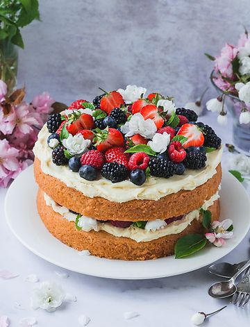 there is a cake with fruit on top and flowers in the backgroung