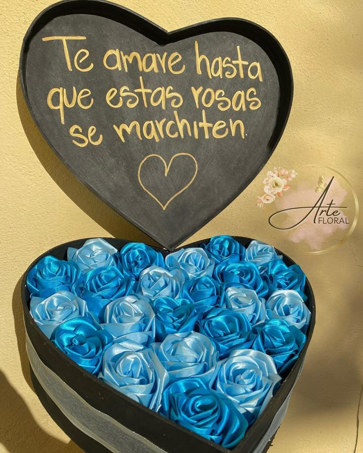 a heart shaped box filled with blue roses next to a sign that says, te amave has que estas yogas se marbatten