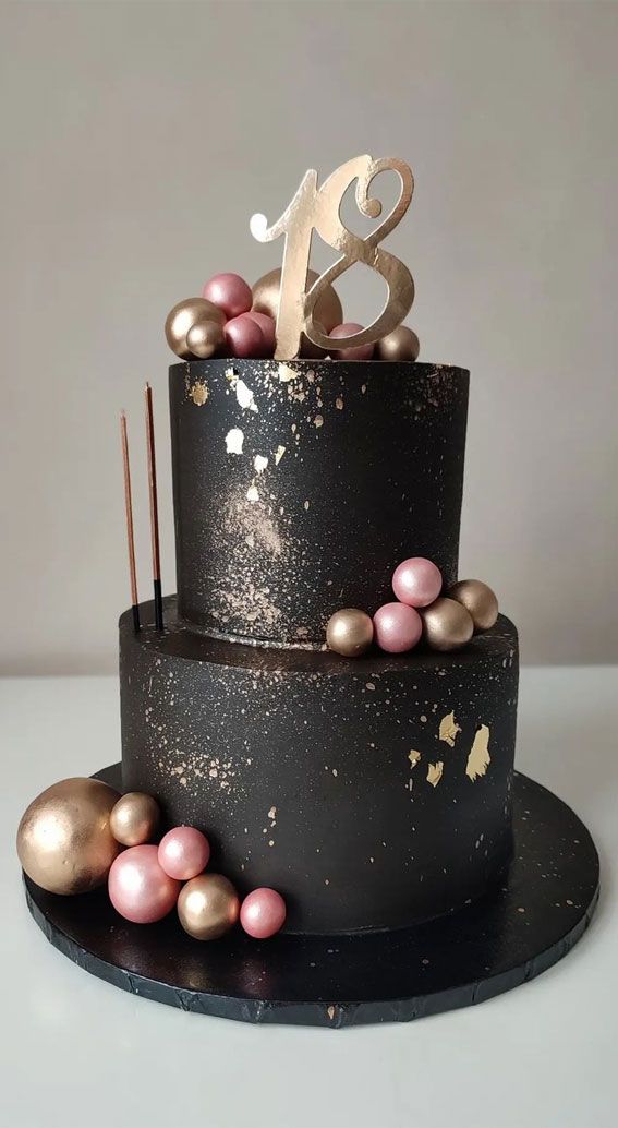 a three tiered cake with gold and pink decorations on the top, sitting on a black plate