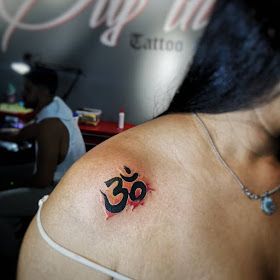 a woman with a tattoo on her shoulder and the word om written in red ink