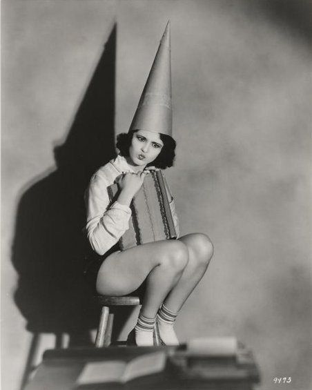 an old photo of a woman sitting on a chair with a cone on her head