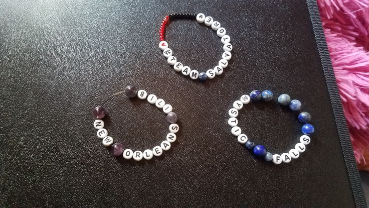 two bracelets made out of beads sitting on top of a table next to a pink feather