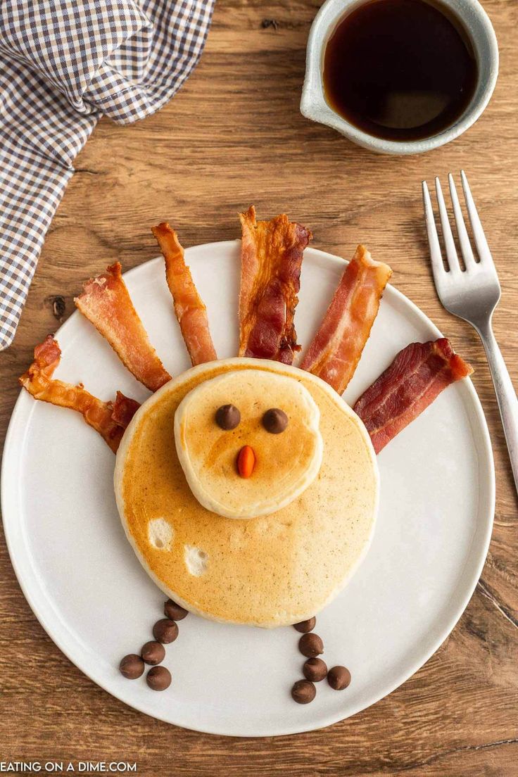 a plate topped with pancakes and bacon on top of a wooden table next to a cup of coffee