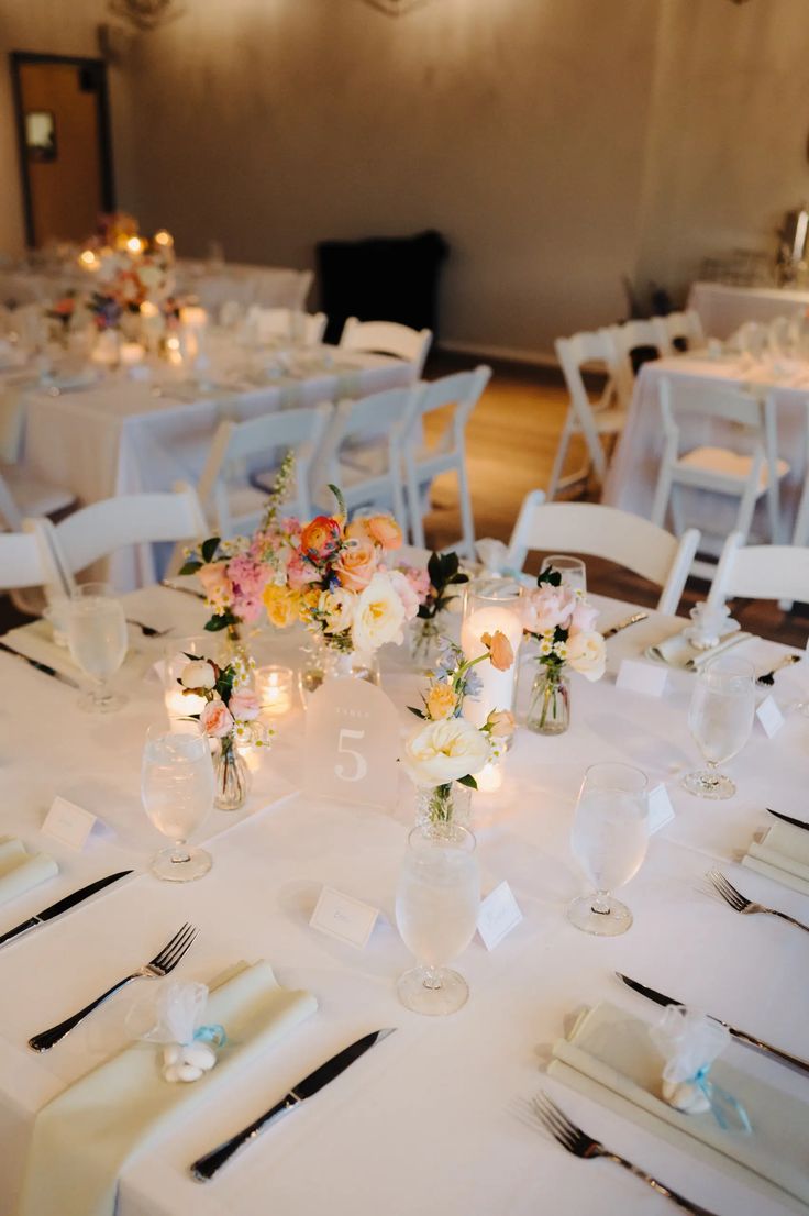 the tables are set with white linens and flowers in vases on each table