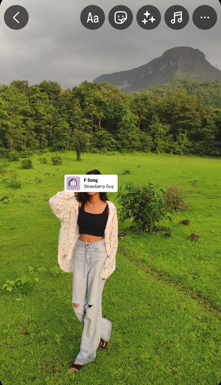 a woman standing on top of a lush green field next to a tall tree covered mountain