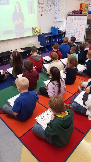 a group of children sitting on the floor in front of a projector screen with an instructor