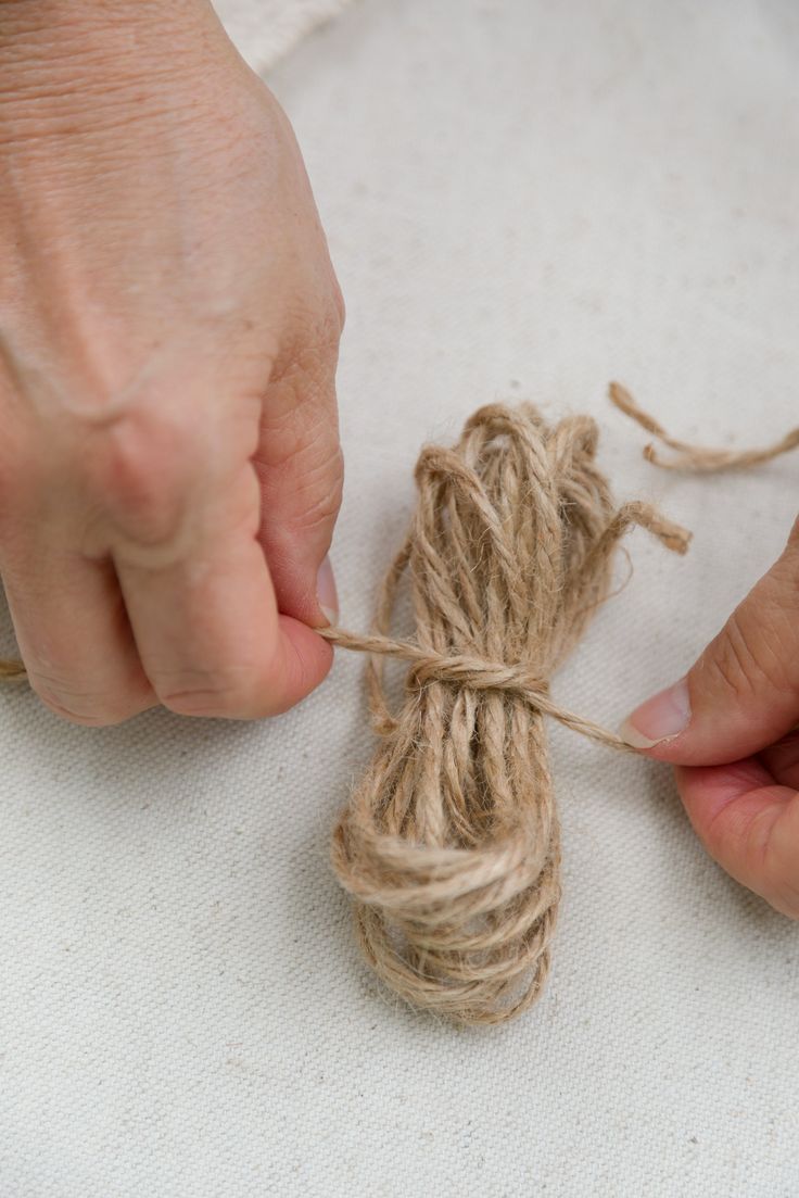 two hands holding twine over a piece of string on a white tablecloth with another person's hand