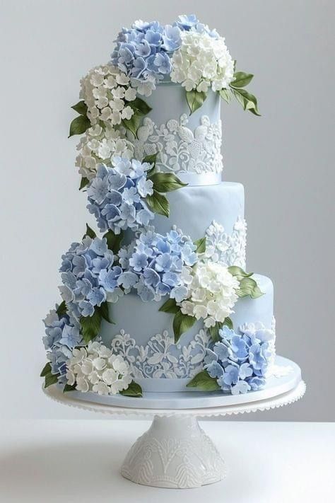 a three tiered blue and white wedding cake with hydrangeas on the side