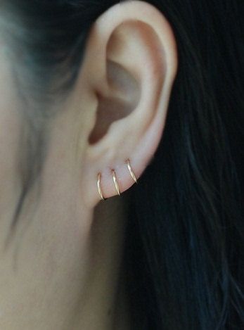 a close up of a woman's ear with two small gold hoop earrings on it