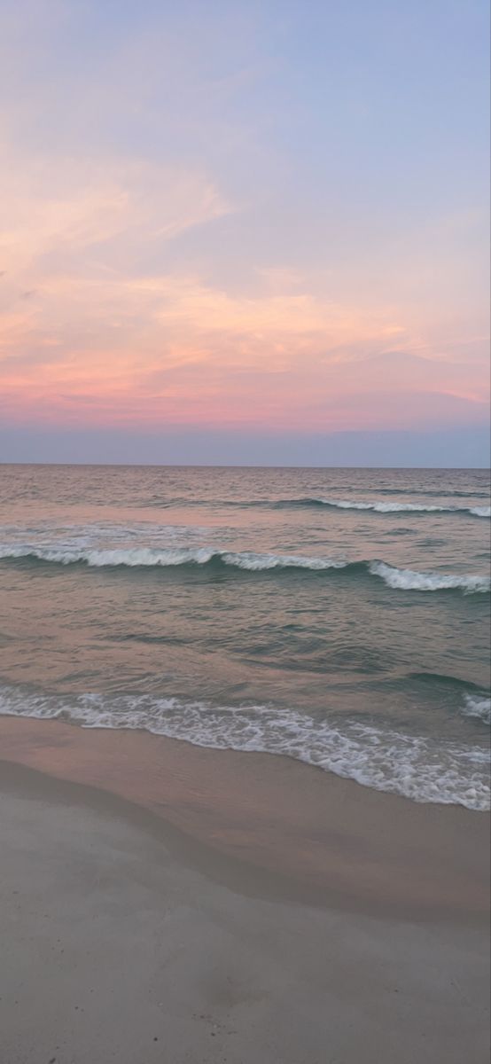 an empty beach with waves coming in to shore and the sun setting on the horizon