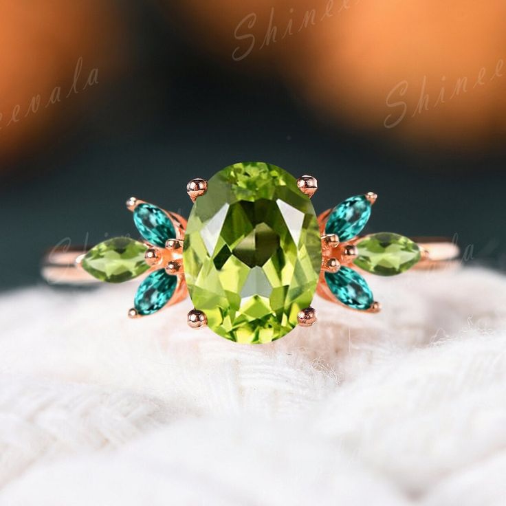 a ring with an oval cut green stone surrounded by two blue and green leaves on top