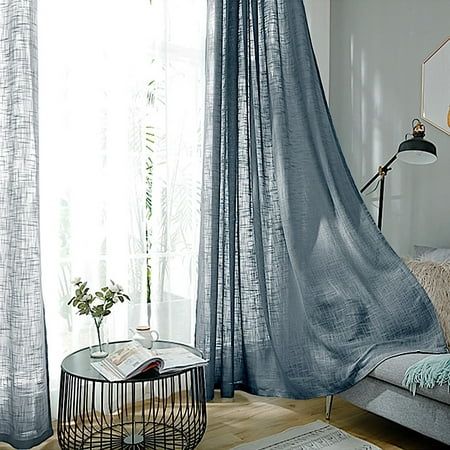 a living room filled with furniture and a window covered in blue sheer curtaining next to a coffee table