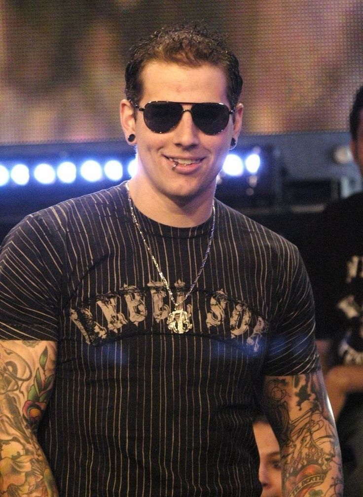 a man with tattoos on his arm wearing sunglasses and smiling at the camera while standing in front of a stage