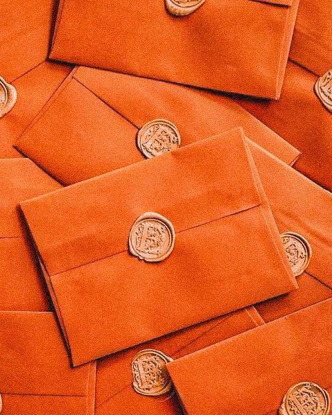 many orange envelopes are stacked on top of each other with gold foil stamping