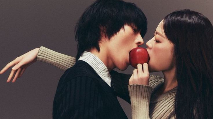 a man and woman kissing while holding an apple