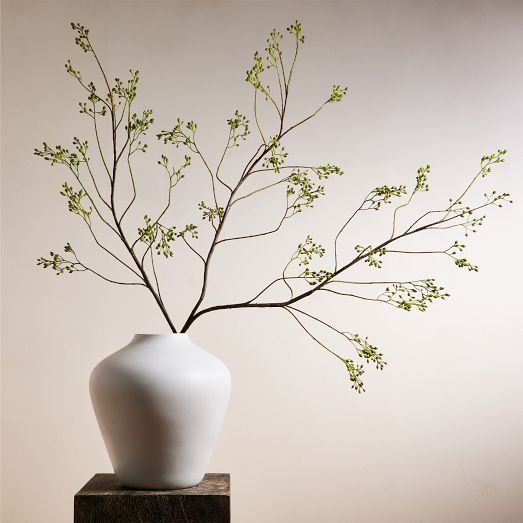 a white vase with green flowers in it on a wooden table next to a wall